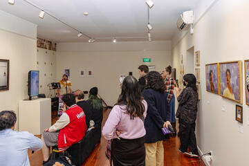 Caryl Loria Illana singing into a microphone on a stand, in the corner of a populated art gallery Caryl Loria Illana singing into a microphone on a stand, in the corner of a populated art gallery