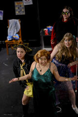 Caryl Loria Illana as Nessper, short light brown wig and green dress, shrugging in front of three other actors leaning out to her sides Caryl Loria Illana as Nessper, short light brown wig and green dress, shrugging in front of three other actors leaning out to her sides