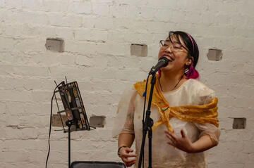 Caryl Loria Illana singing into a microphone on a stand, smiling Caryl Loria Illana singing into a microphone on a stand, smiling