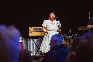 Caryl Loria Illana singing into a microphone, looking out at the audience Caryl Loria Illana singing into a microphone, looking out at the audience