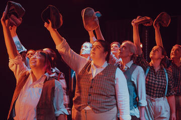 Caryl Loria Illana as a Newsie in Miscast, raising her newsboy hat