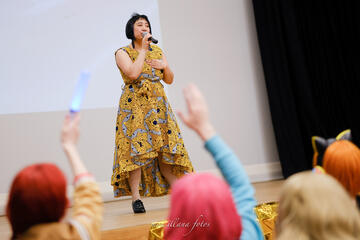 Caryl Loria Illana singing onstage with audience waving lightsticks in foreground Caryl Loria Illana singing onstage with audience waving lightsticks in foreground