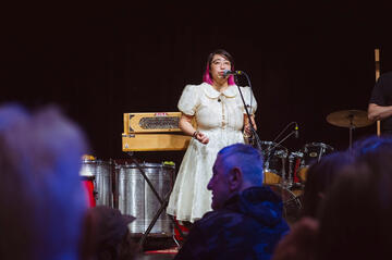 Caryl Loria Illana singing into a microphone, looking out at the audience Caryl Loria Illana singing into a microphone, looking out at the audience