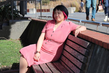 Caryl Loria Illana in a pink dress, sitting on a bench, smiling slightly at camera