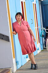 Caryl Loria Illana in a pink dress, leaning against a blue boat shed